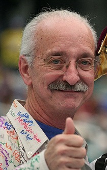 Close-up of Dr. Woodie Flowers smiling and giving a thumbs up in a signed shirt