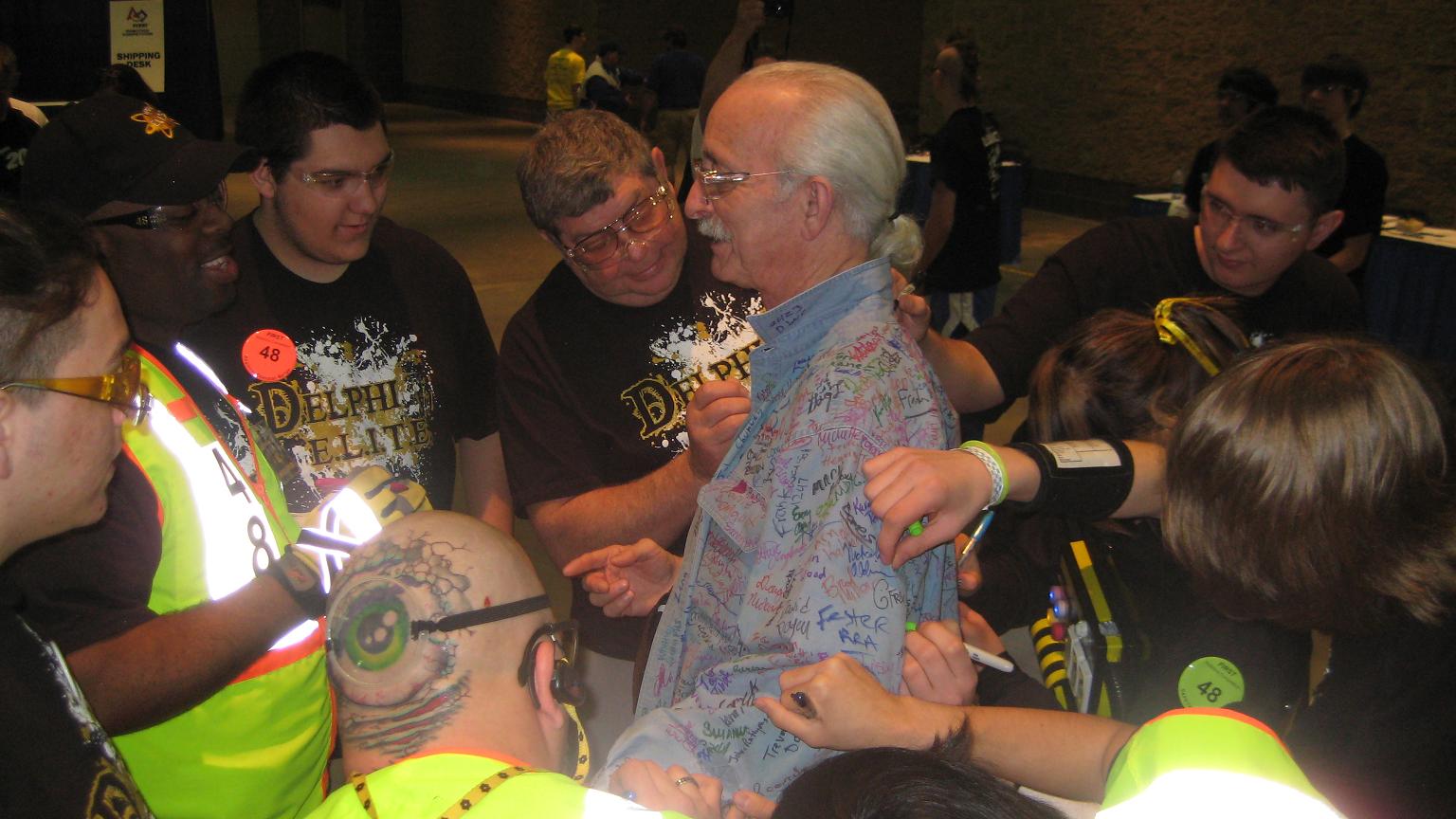Students and mentors signing Dr. Woodie Flowers' shirt at a competition event