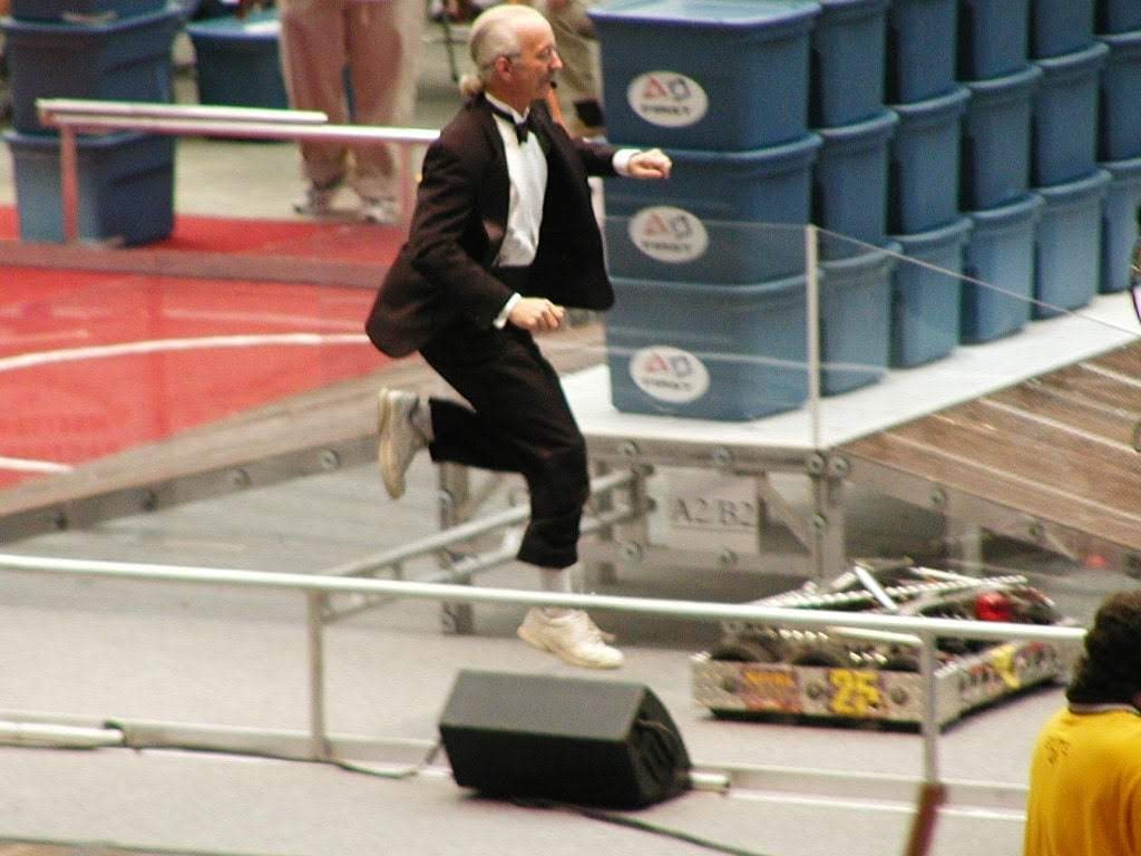Dr. Woodie Flowers wearing a tuxedo and jumping over a rail onto the competition field